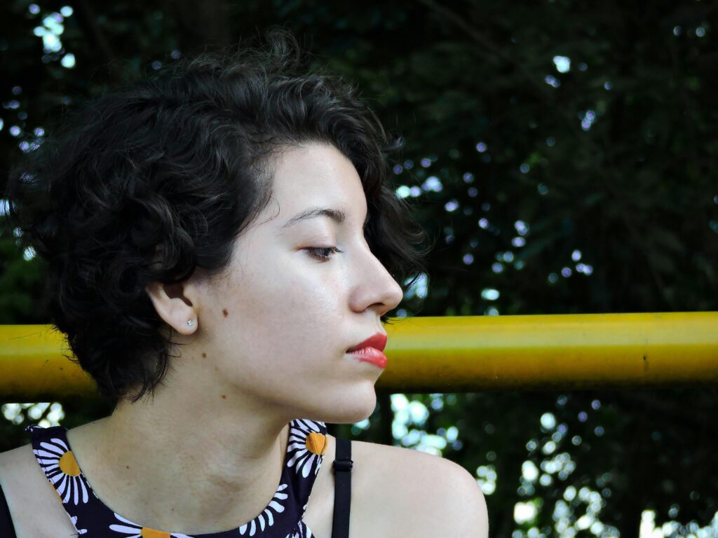 Profile portrait of a young woman with short curly hair, enjoying leisure outdoors.